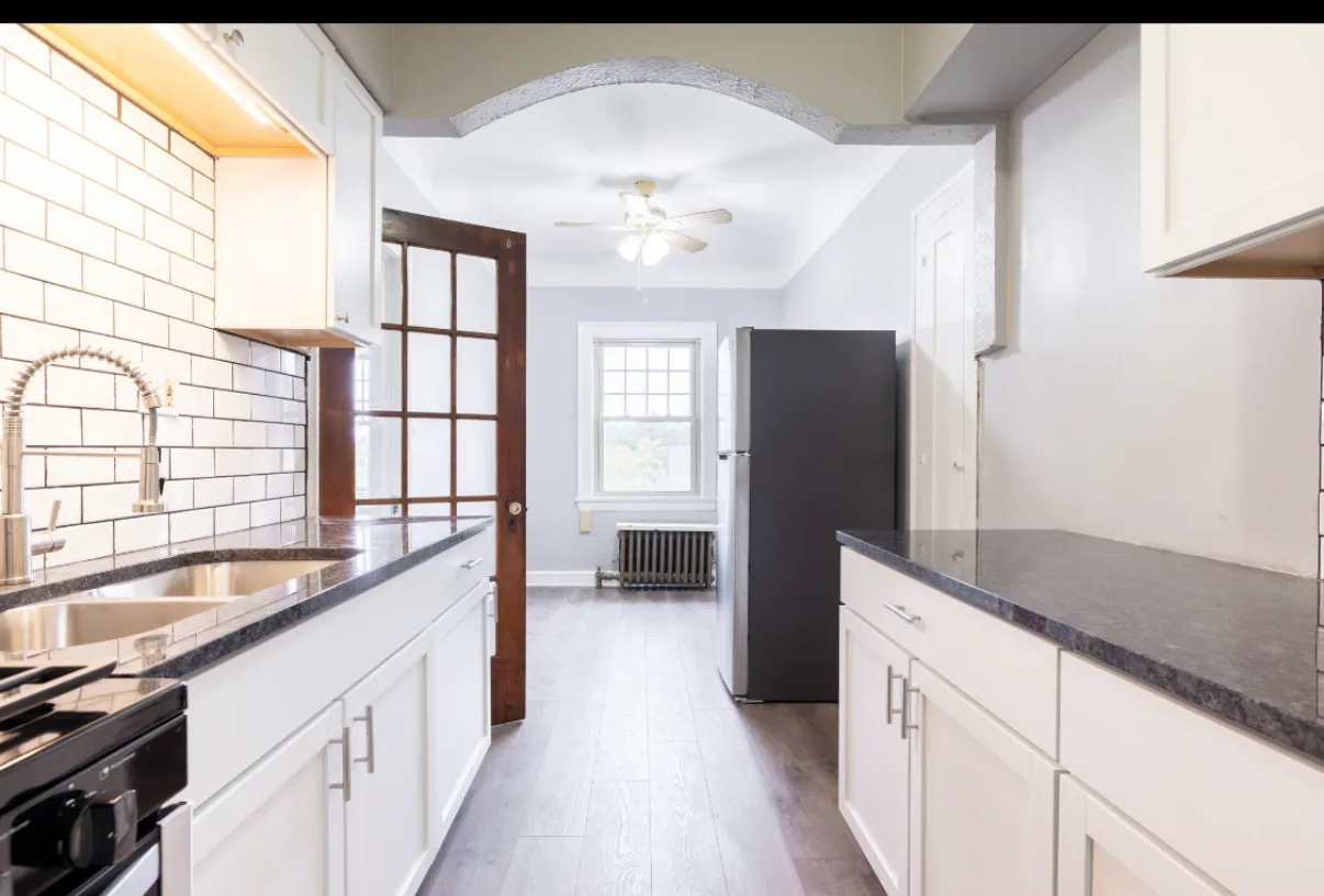 Galley kitchen with white subway tile, dark counters and an original wood and glass door